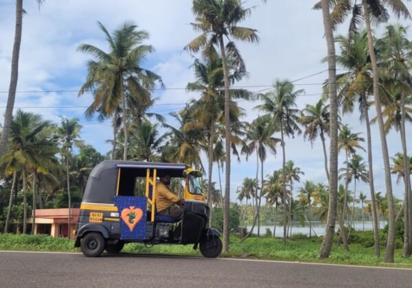 A tuk tuk in Kollam, Kerala, showcasing its bright design against a backdrop of bustling local life and tropical scenery.