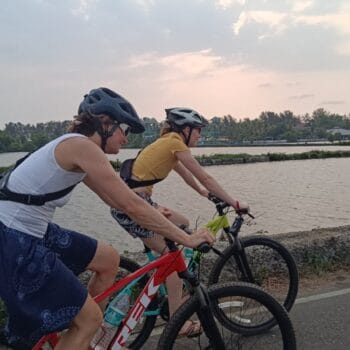 Two people cycling along a road beside fish farms in Cherai's rural village.