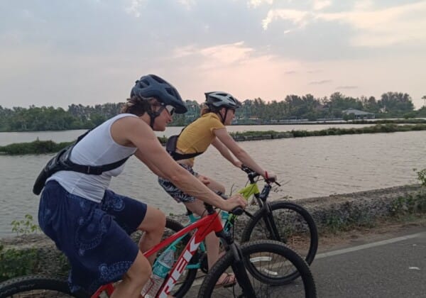 Two people cycling along a road beside fish farms in Cherai's rural village.