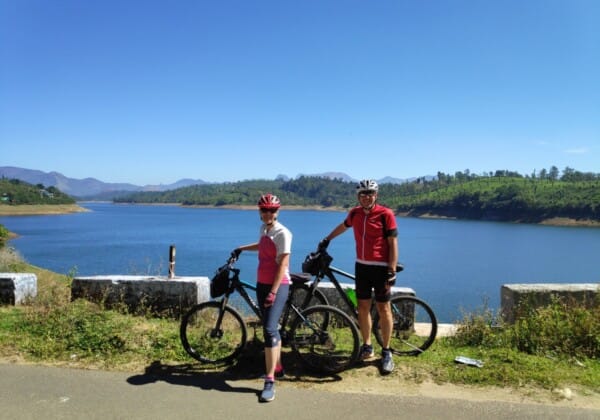 Two people beside their bikes near lake, taking in the beautiful scenery at Sholayar Dam in Valparai, Tamil Nadu.