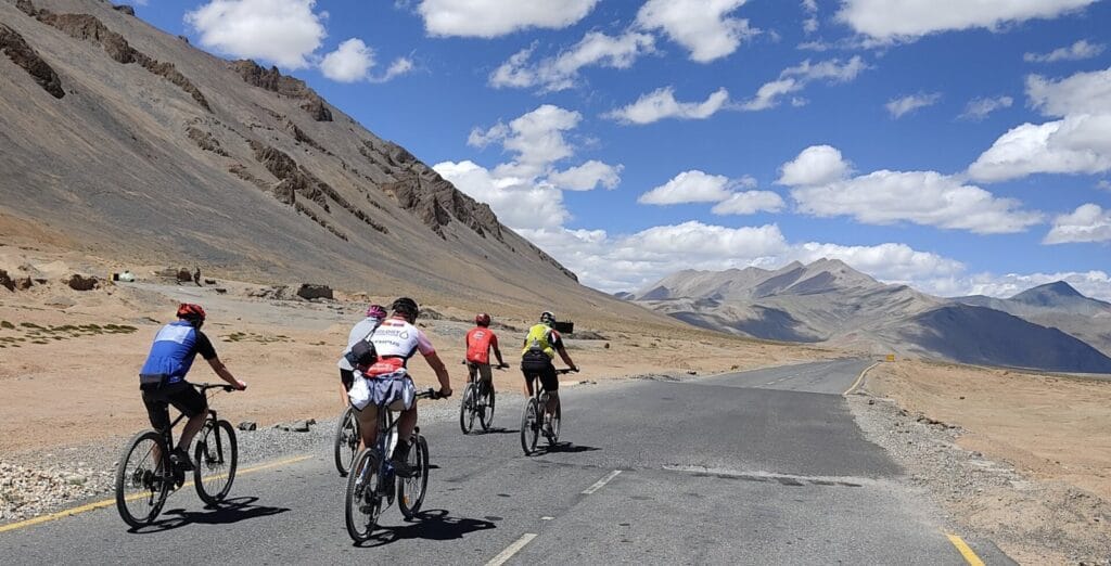 Three cyclists ride along a mountain road during the Manali to Leh cycling adventure.