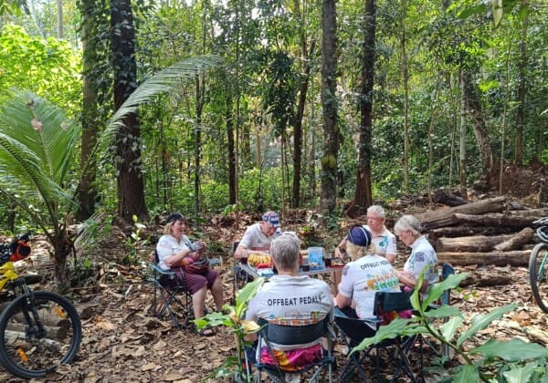 A group of cyclists resting around a table in a lush forest in the Western Ghats.