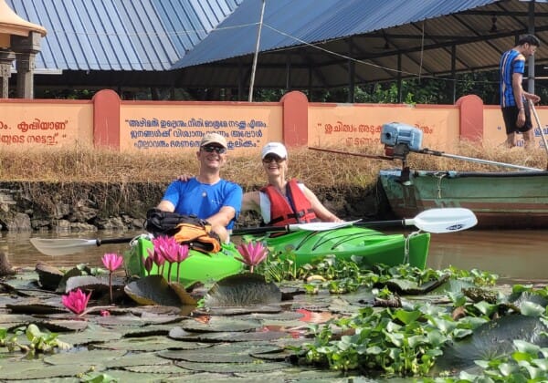 A couple poses in a kayak on a canal surrounded by vibrant water lilies during their kayaking adventure in Allepey.