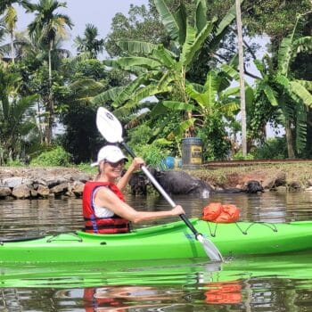 A woman paddles a green kayak in the calm waters of Alleppey, immersed in the beauty of her surroundings.
