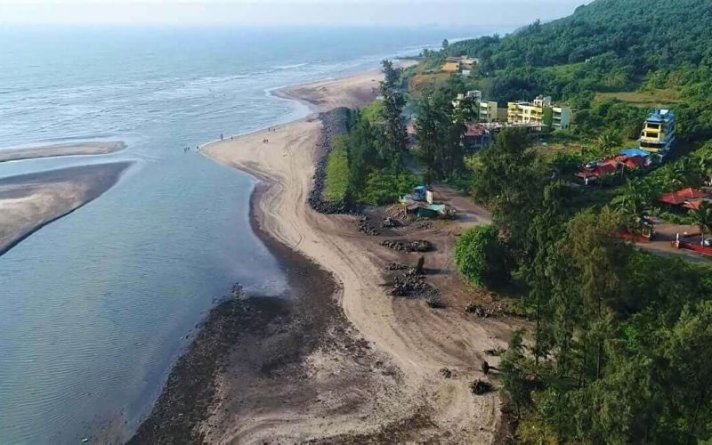 35 Aerial view of a coastal tropical landscape with a long sandy beach, lush green vegetation, and buildings along the shoreline. The image shows the natural beauty of the coastal environment with the ocean in the background.